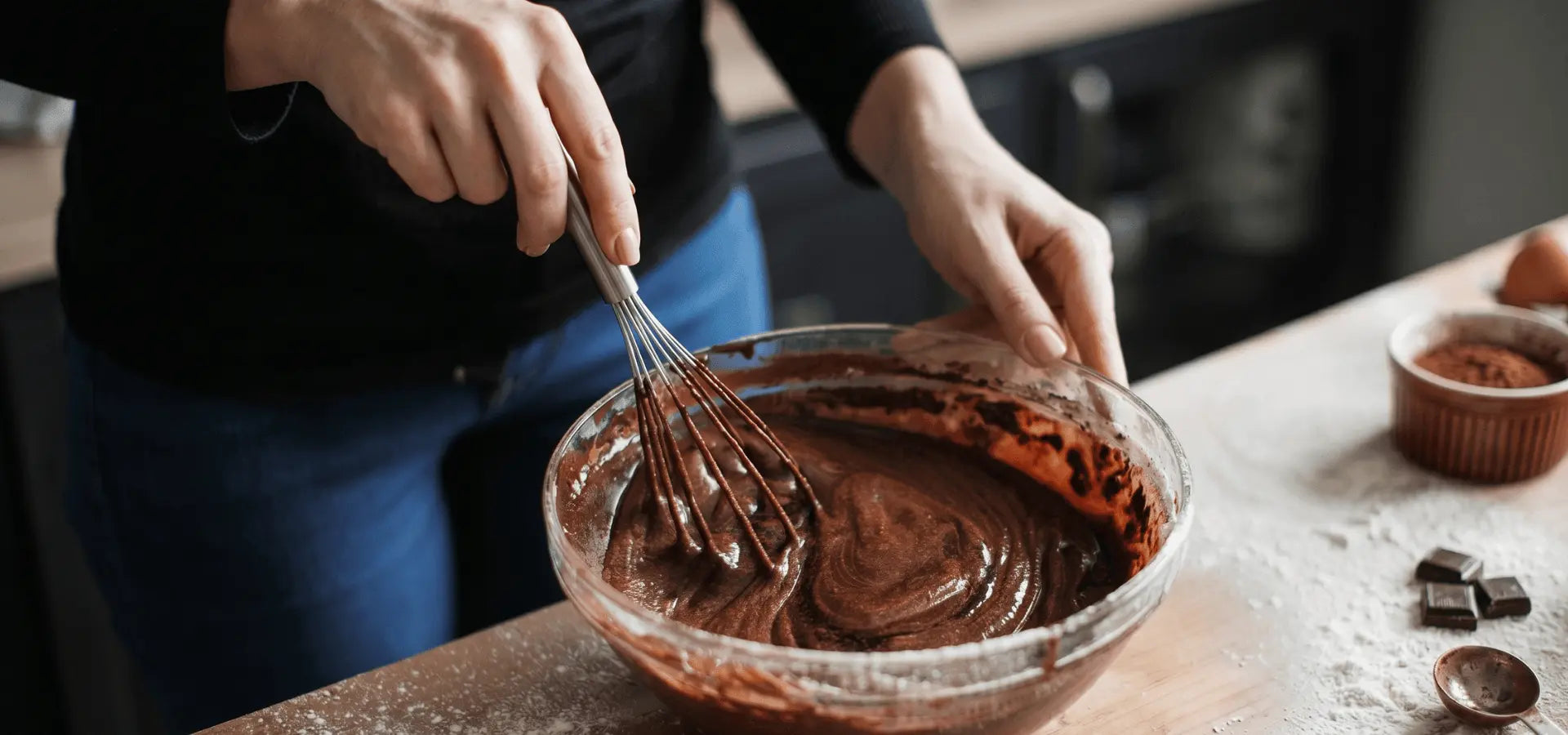 Person mixing chocolate batter in a bowl with a whisk on a kitchen counter.