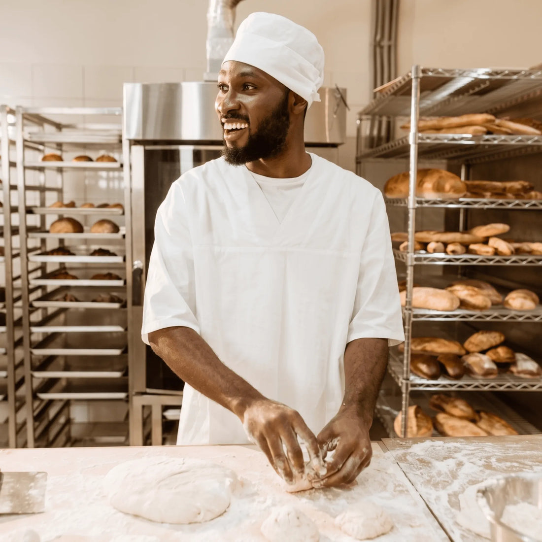 Baker kneading dough in a bakery with shelves of bread in the background